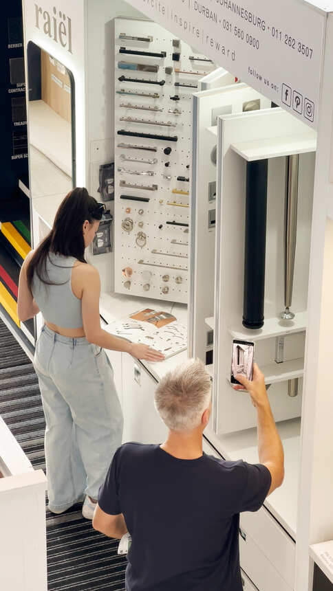 A student examining cabinet handles on a hardware display wall while another visitor photographs it