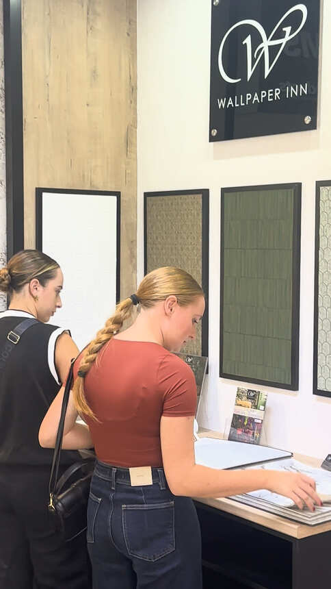 Students paging through wallpaper sample books at a wallpaper display