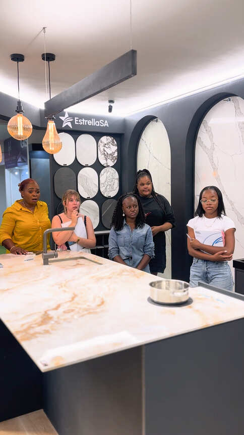 Students listening around a stone-topped kitchen island at a surfaces display